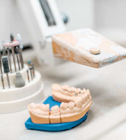 A dental lab technician works on a prosthetic with 3D printing equipment in the background